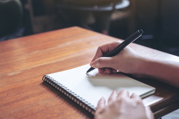 mano escribiendo en un cuaderno en blanco blanco sobre mesa de madera