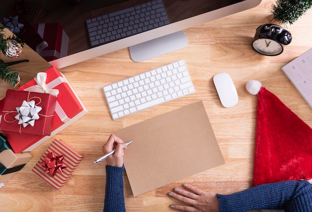 Mano escribiendo maqueta tarjeta de felicitación para feliz Navidad y feliz con decoración de Navidad en escritorio.