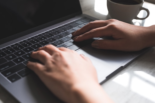 Mano escribiendo en el teclado del ordenador portátil con una taza de café sobre la mesa