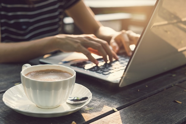 Mano escribiendo en teclado portátil con taza de café