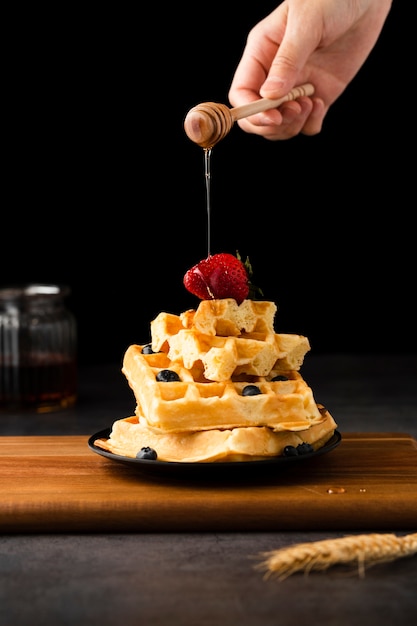 Mano esparciendo miel sobre waffles con frutas