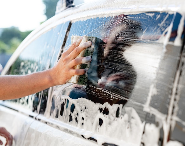 Mano con esponja y espuma para lavar la ventana del coche