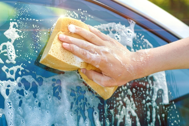 Una mano con una esponja lava la ventana de un auto