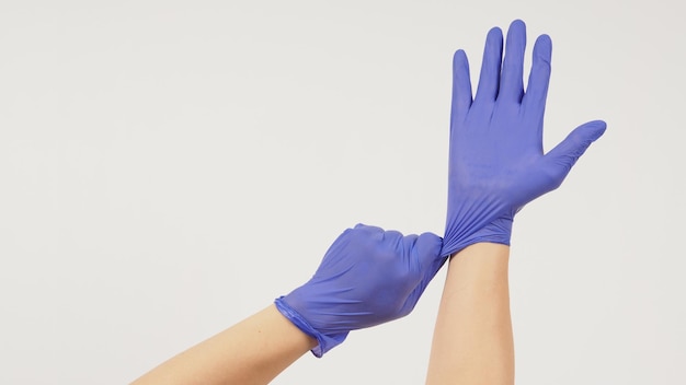 La mano está tirando de guantes de látex morados sobre fondo blanco.