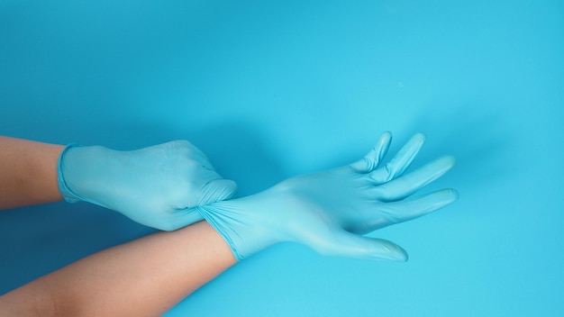 La mano está tirando de guantes de médico o guantes de látex azul de la mano derecha sobre fondo azul.