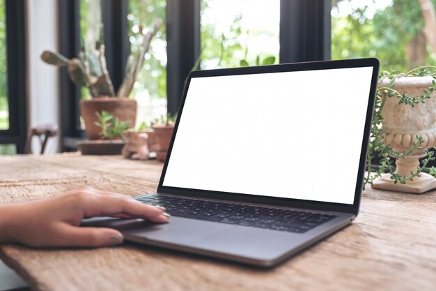 Una mano está usando y tocando una computadora portátil con una pantalla de escritorio en blanco sobre una mesa de madera