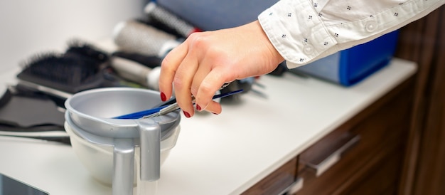 Mano de estilista prepara tinte en un recipiente para teñir el cabello en la peluquería