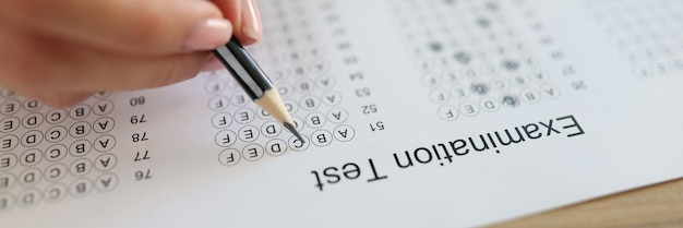 La mano del estudiante sostiene un lápiz sobre papel con preguntas de prueba. La mujer toma el examen en la universidad y elige las respuestas correctas.