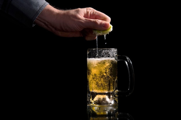 mano exprimiendo un limón en un frasco de vidrio con cerveza refrescante sobre un fondo negro