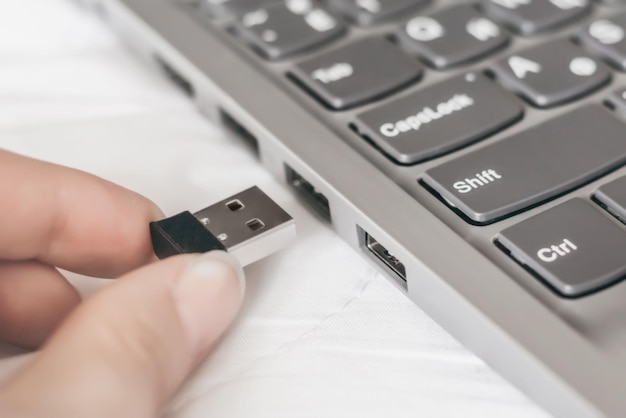 La mano de Famele inserta el dispositivo adaptador universal Receptor en el puerto USB de la computadora portátil