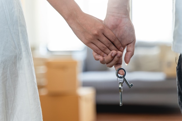 Mano de la feliz pareja joven hombre y mujer entregando sus nuevas llaves de casa delante de una puerta de casa abierta