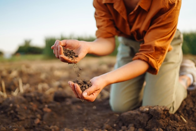 La mano femenina del agricultor experto recoge el suelo y comprueba la salud del suelo antes del crecimiento de una semilla de verdura