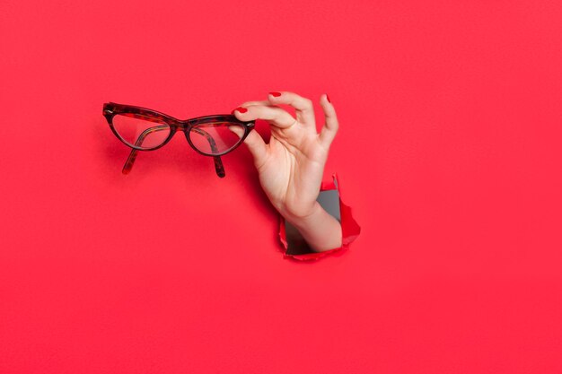 Foto mano femenina en agujero de papel con gafas