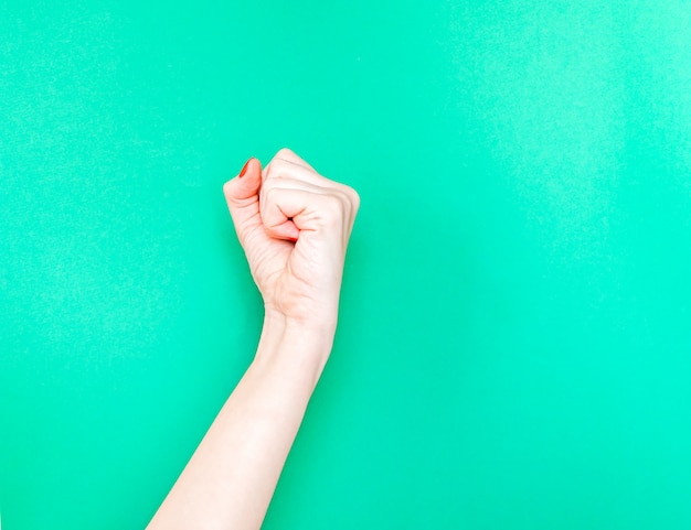 La mano femenina con apretó un puño en fondo aislado del color verde de la turquesa.