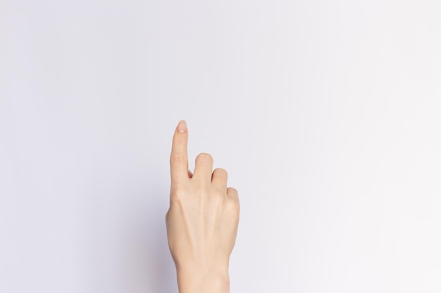 Mano femenina apuntando hacia arriba con el dedo índice de primer plano en un fondo blanco vacío