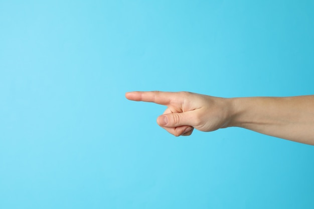 Mano femenina apuntando sobre fondo azul, espacio para texto