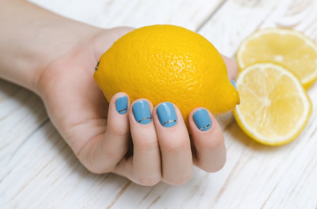 Foto mano femenina con arte de uñas azul claro con limón.