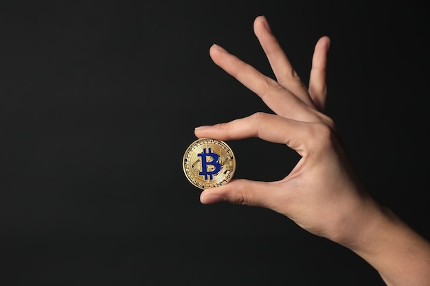 Foto mano femenina con bitcoin dorado en un fondo oscuro