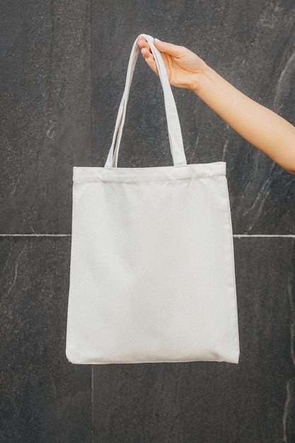 Mano femenina en la calle sosteniendo una bolsa ecológica blanca simulada