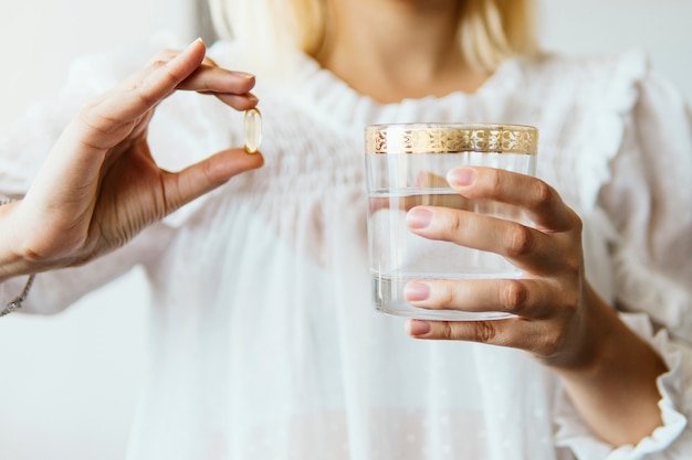 Mano femenina con cápsula de suplemento de aceite de pescado Omega 3 y vaso de agua