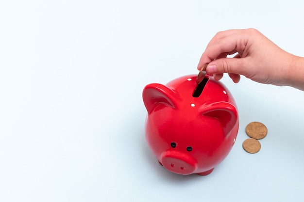 Mano femenina caucásica pone una moneda en una hucha roja junto a monedas de mentira