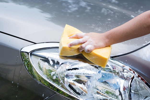 Mano femenina con coche de lavado de esponja amarilla