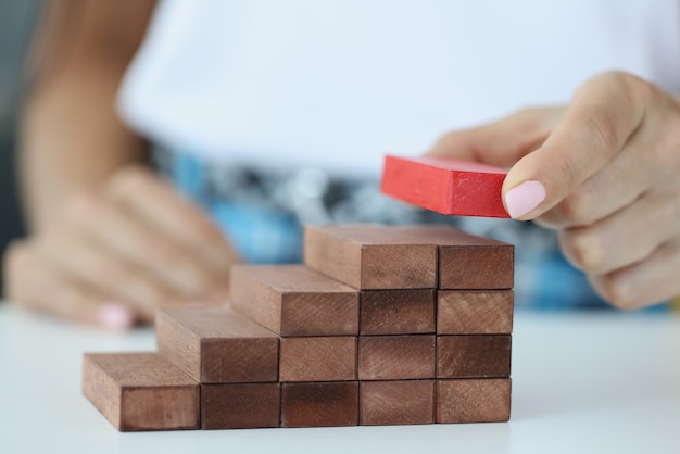 Foto mano femenina construye escalera de bloques de madera desde arriba rojo