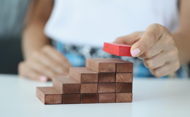 Mano femenina construye escalera de bloques de madera desde arriba rojo