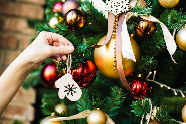 La mano femenina cuelga en el juguete de madera del árbol de navidad. Preparándose para el nuevo año.