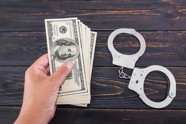 Foto mano femenina da dinero en el fondo de una mesa de madera y esposas. concepto de crimen y soborno.