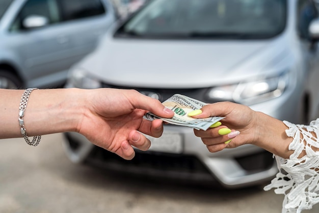 La mano femenina le da un dólar a un vendedor al comprar un auto nuevo y moderno