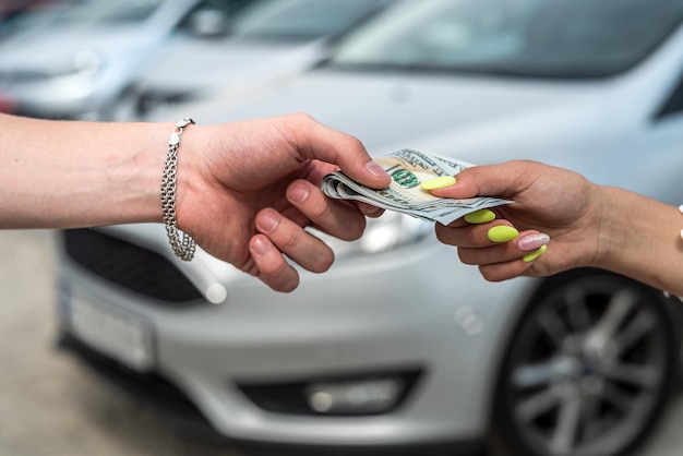 Mano femenina da dólar a un vendedor al comprar un automóvil nuevo y moderno, concepto de venta