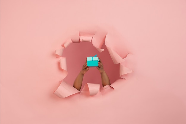 Mano femenina dando regalo en agujero de papel rosa coral rasgado