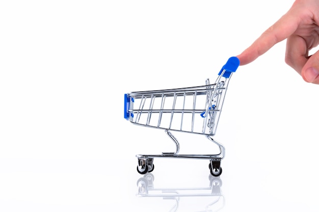 Mano femenina con los dedos empujando un carrito de compras aislado sobre fondo blanco. Copie el espacio.