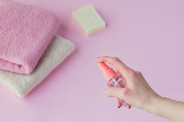 Mano femenina con desinfectante antibacteriano para manos sobre fondo rosa claro.