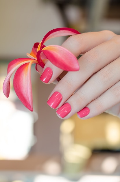Mano femenina con diseño de uñas rosa con flor rosa.