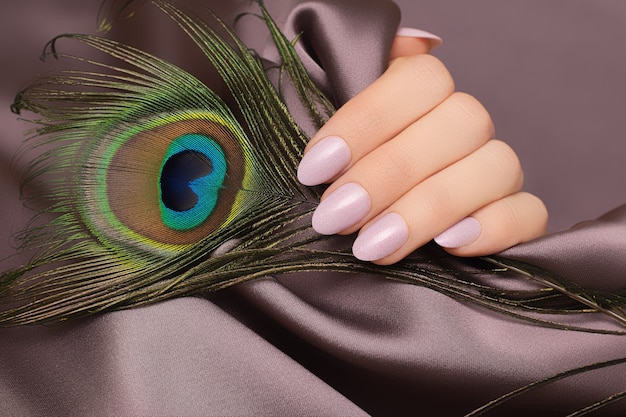 Mano femenina con diseño de uñas rosa con pluma de pavo real.