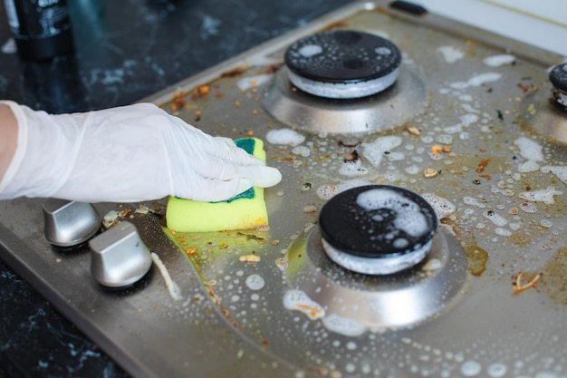 Mano femenina doméstica con guantes limpiando la estufa sucia después de cocinar usando una esponja para lavar Mujer ama de casa disfrutando de la vista superior del primer plano del hogar diario