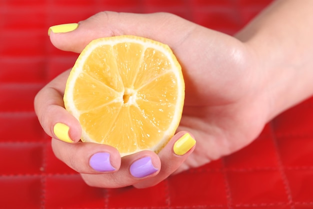 Foto mano femenina con elegantes uñas coloridas sosteniendo limón fresco sobre fondo de color