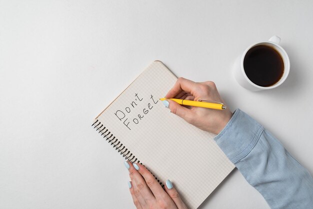 Mano femenina escribe en un aviso de cuaderno No olvides el café de la mañana y el concepto de planes