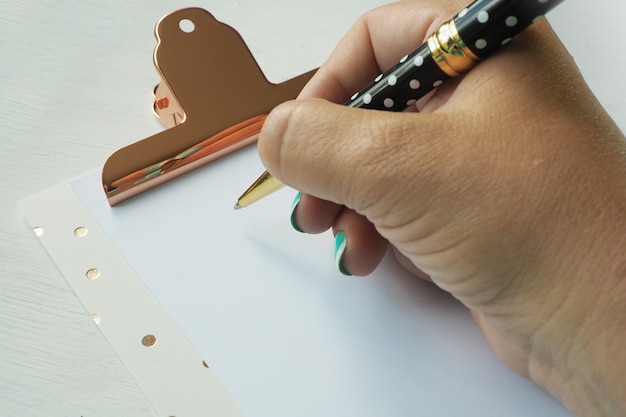 La mano femenina escribe con un bolígrafo en una hoja de papel limpia en un sujetapapeles.