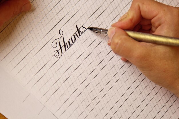 la mano femenina escribe con la pluma de tinta la palabra gracias en una hoja de papel blanco con rayas papelería en el escritorio vista superior lecciones de ortografía y ejercicios de caligrafía Fondo de diseño de plantilla