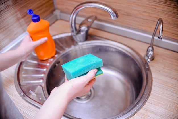 Mano femenina con esponja de plato con jabón para lavar platos. Concepto de limpieza de la casa.