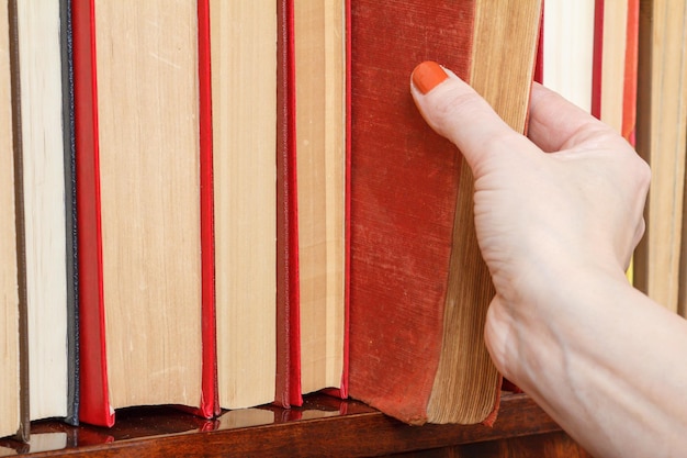 Mano femenina está tomando un libro viejo de la estantería Muchos libros de tapa dura en estante de madera