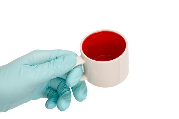 Mano femenina en guante de látex sosteniendo una taza vacía sobre un fondo blanco aislado