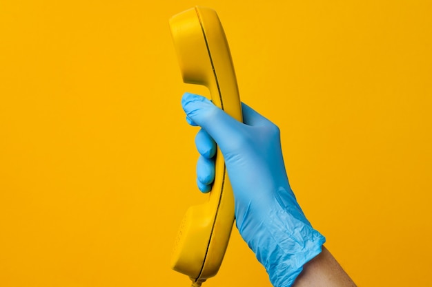 Mano femenina en guante médico sosteniendo altavoz de teléfono amarillo