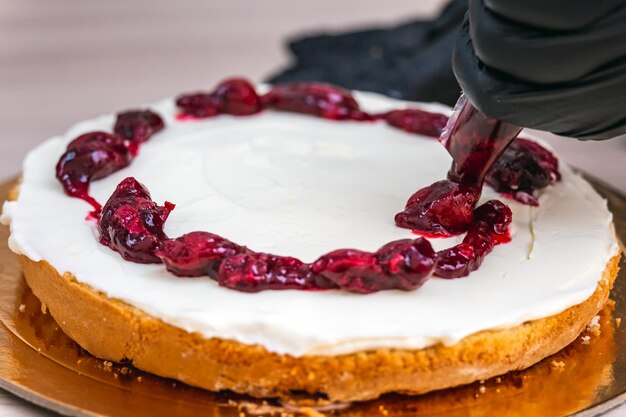 Foto mano femenina con guante negro exprime confitura de cereza en un pastel de queso con coco