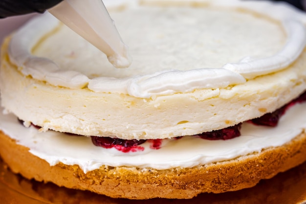 Mano femenina en guante negro exprime la crema en un pastel de queso con coco