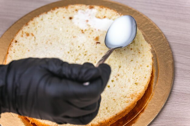 Foto mano femenina con guante negro vierte leche en un pastel de queso con coco en una mesa de madera