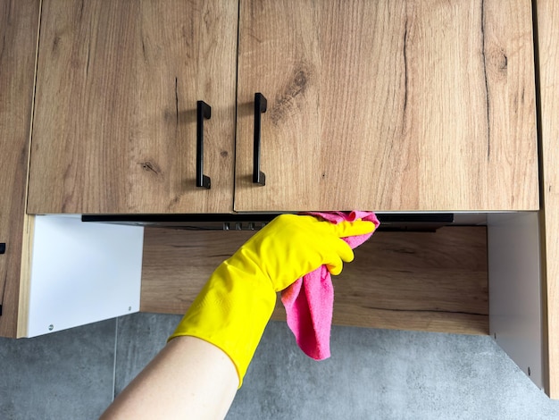 mano femenina en guantes de goma amarillos usando un trapo limpiando la cocina de madera superior